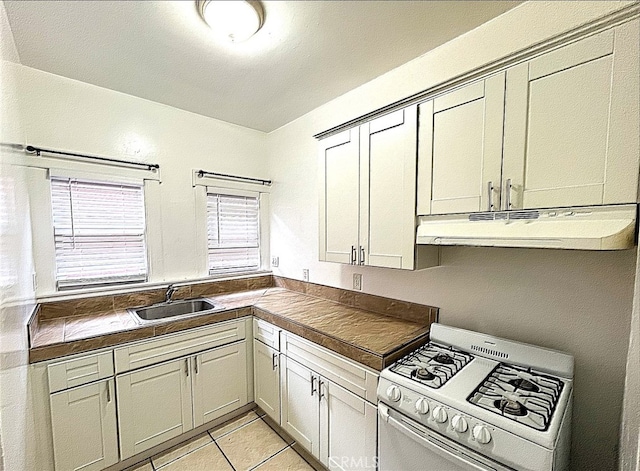 kitchen featuring under cabinet range hood, a sink, dark countertops, white gas range oven, and light tile patterned flooring