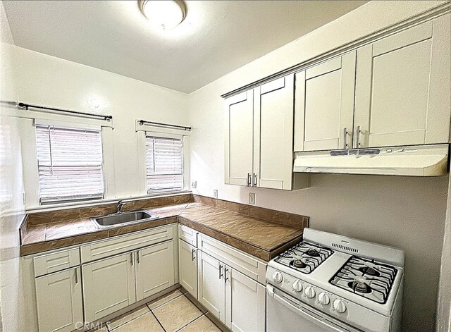 332 W 9th St, Long Beach, CA 90813 - kitchen with light tile patterned floors, a sink, dark countertops, under cabinet range hood, and gas range gas stove