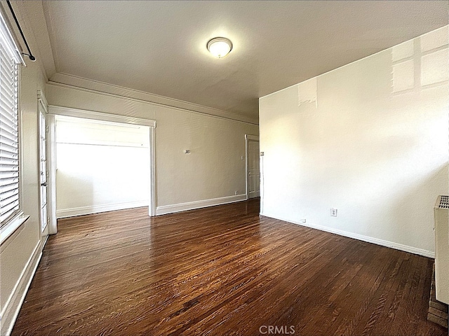 empty room with crown molding, baseboards, and dark wood-style flooring