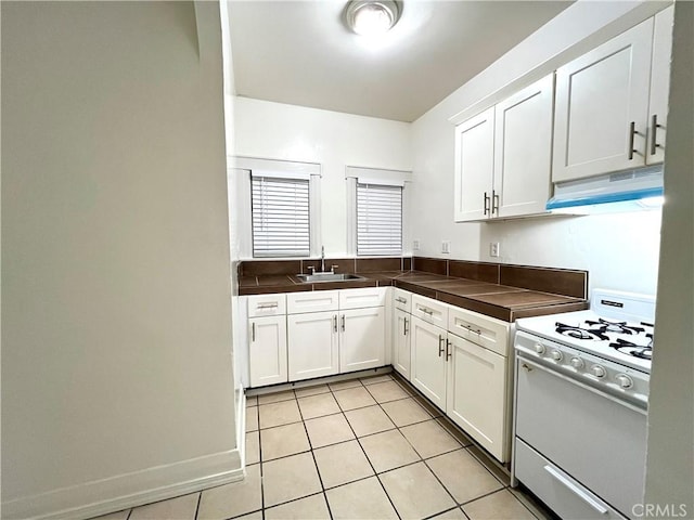 kitchen featuring under cabinet range hood, a sink, white cabinets, light tile patterned flooring, and white gas range