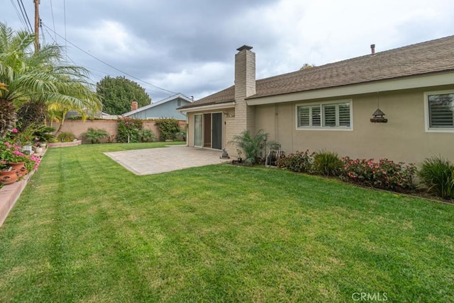 rear view of property with fence, stucco siding, a chimney, a yard, and a patio area