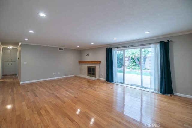 unfurnished living room with a glass covered fireplace, baseboards, visible vents, and light wood finished floors