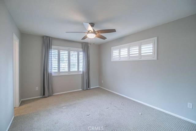 carpeted spare room with a ceiling fan and baseboards