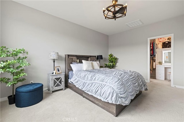 bedroom with visible vents, light carpet, a walk in closet, baseboards, and a notable chandelier
