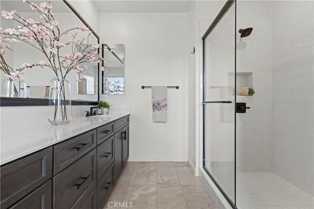 full bath with baseboards, tiled shower, and vanity