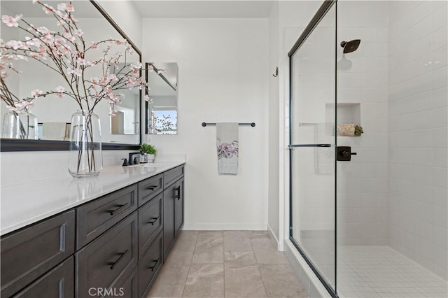full bath with vanity, baseboards, and a tile shower