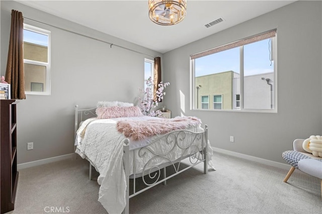 carpeted bedroom with a notable chandelier, visible vents, and baseboards