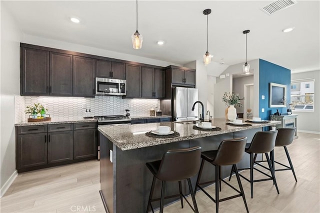 kitchen featuring tasteful backsplash, a kitchen breakfast bar, light wood-style floors, visible vents, and appliances with stainless steel finishes