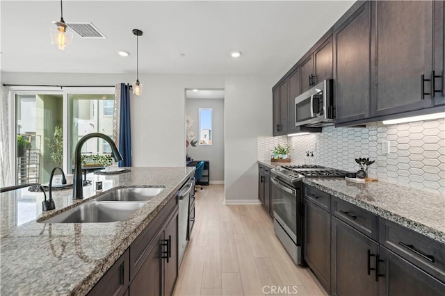 kitchen with dark brown cabinets, decorative backsplash, stone counters, stainless steel appliances, and a sink