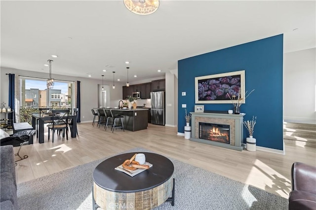 living room with a glass covered fireplace, recessed lighting, light wood-type flooring, and baseboards