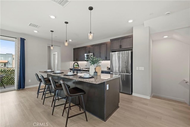 kitchen with dark brown cabinetry, a kitchen breakfast bar, visible vents, stainless steel appliances, and a center island with sink