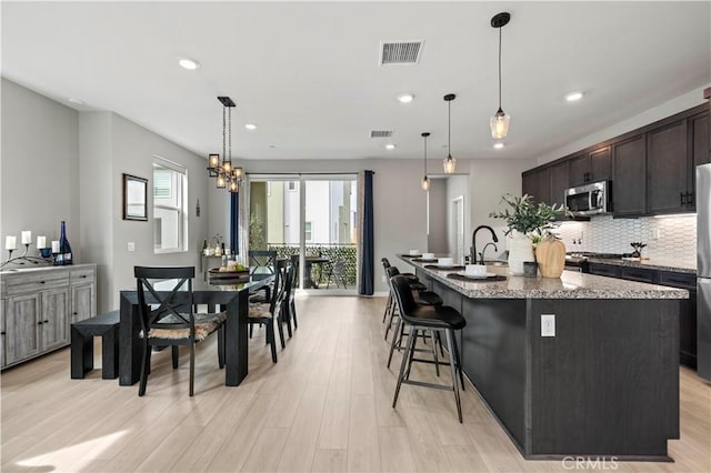 kitchen with stone countertops, recessed lighting, an island with sink, visible vents, and stainless steel appliances
