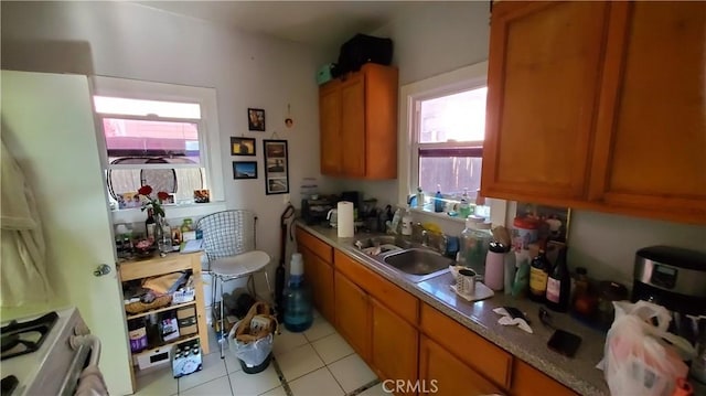 kitchen featuring brown cabinetry, a sink, light tile patterned floors, and stainless steel gas stove