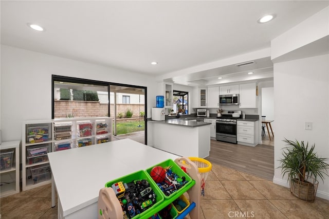 kitchen with dark countertops, recessed lighting, stainless steel appliances, a peninsula, and white cabinets