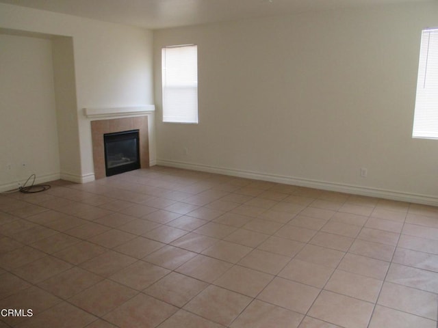 unfurnished living room with light tile patterned floors, baseboards, a healthy amount of sunlight, and a tile fireplace