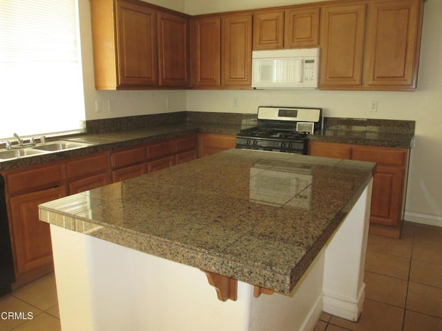 kitchen featuring light tile patterned floors, tile counters, white microwave, and stainless steel range with gas cooktop