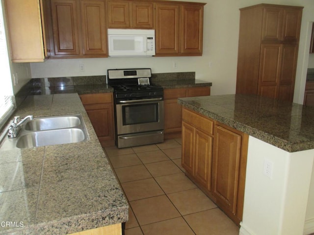 kitchen featuring stainless steel gas range oven, a sink, light tile patterned floors, white microwave, and tile counters