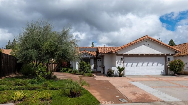 mediterranean / spanish-style house featuring roof mounted solar panels, fence, concrete driveway, an attached garage, and a tiled roof