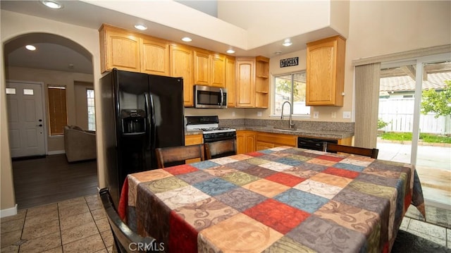 kitchen with a sink, light brown cabinets, arched walkways, black appliances, and open shelves