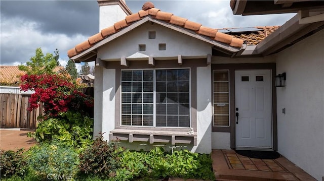 doorway to property featuring stucco siding, fence, a chimney, and a tile roof