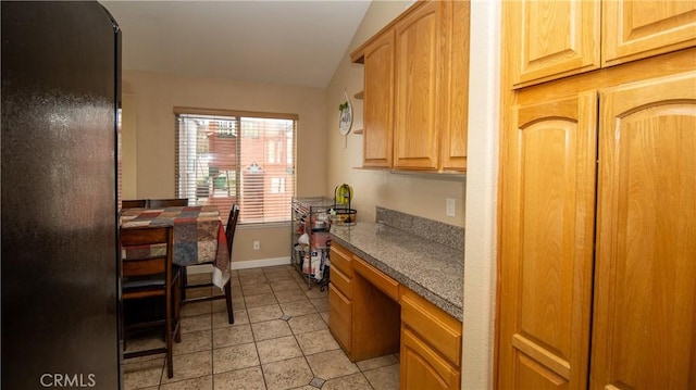 kitchen with baseboards, light tile patterned flooring, vaulted ceiling, built in desk, and dark countertops