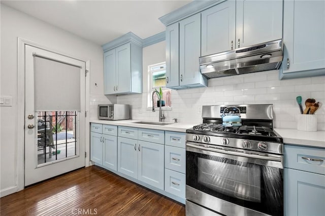 kitchen featuring dark wood finished floors, a sink, stainless steel appliances, light countertops, and under cabinet range hood