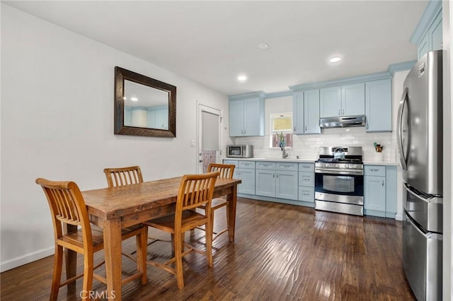 kitchen with dark wood-style flooring, light countertops, under cabinet range hood, appliances with stainless steel finishes, and tasteful backsplash