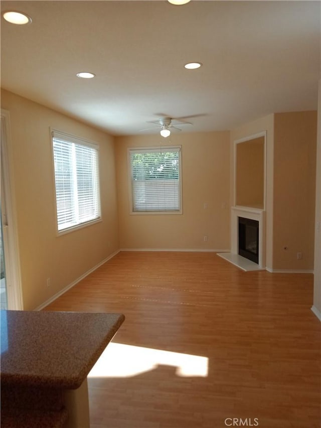 unfurnished living room with baseboards, ceiling fan, recessed lighting, light wood-style floors, and a glass covered fireplace