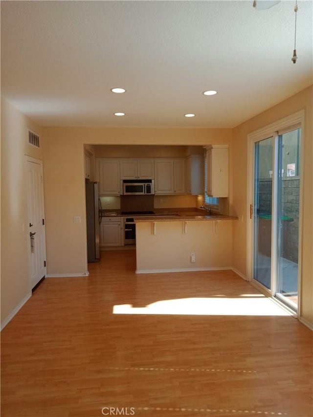 kitchen with a kitchen bar, visible vents, stainless steel appliances, light wood-style floors, and a peninsula