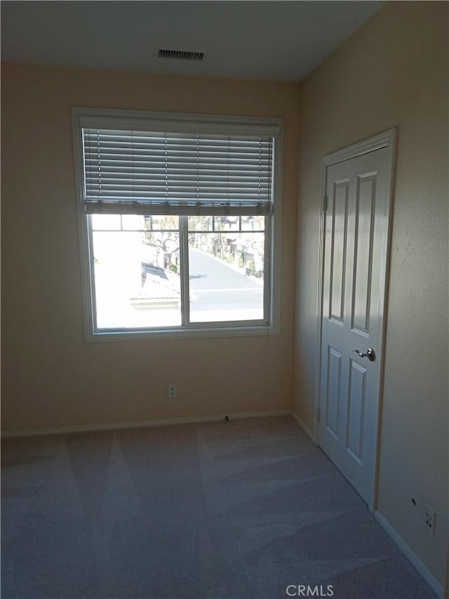 spare room featuring a wealth of natural light, visible vents, baseboards, and carpet