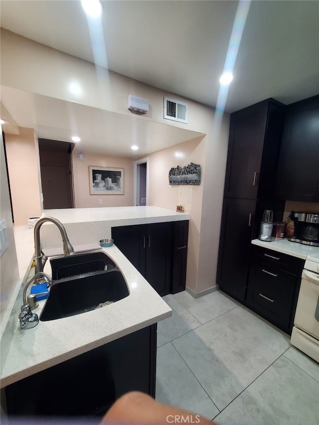 kitchen with a sink, visible vents, dark cabinetry, and white range with electric cooktop