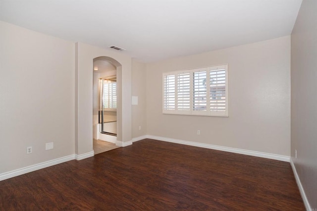 unfurnished room with baseboards, arched walkways, visible vents, and wood finished floors