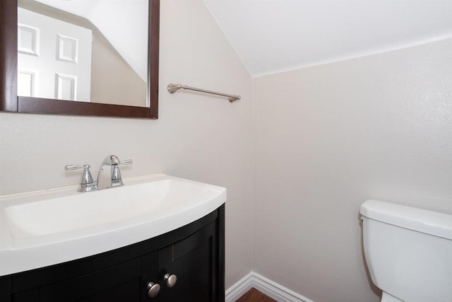 half bath featuring toilet, vanity, and vaulted ceiling