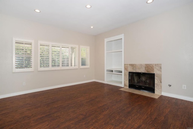 unfurnished living room with baseboards, built in shelves, wood finished floors, and a fireplace