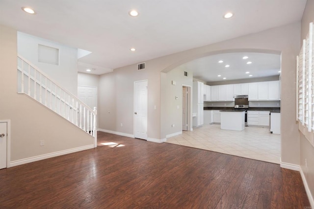 unfurnished living room with recessed lighting, arched walkways, and light wood finished floors