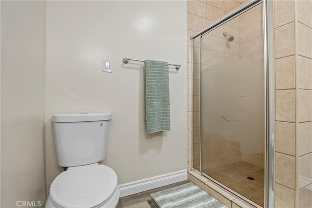 bathroom featuring a stall shower, toilet, baseboards, and wood finished floors