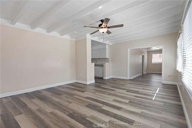 unfurnished living room with a ceiling fan, beam ceiling, wood finished floors, and baseboards