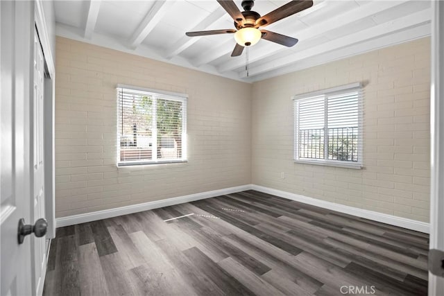 empty room with beam ceiling, brick wall, baseboards, and dark wood-style flooring