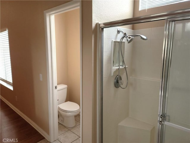 bathroom featuring tile patterned floors, a shower stall, toilet, and baseboards