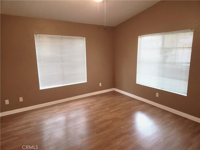 unfurnished room featuring baseboards, lofted ceiling, and wood finished floors