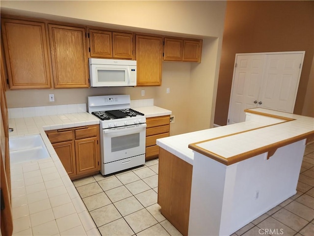 kitchen featuring a sink, white appliances, brown cabinetry, light tile patterned floors, and tile counters