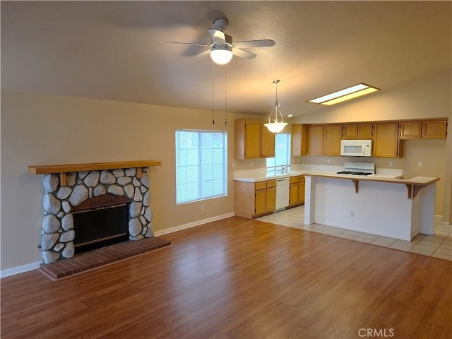 kitchen with light wood finished floors, light countertops, lofted ceiling, a stone fireplace, and white appliances