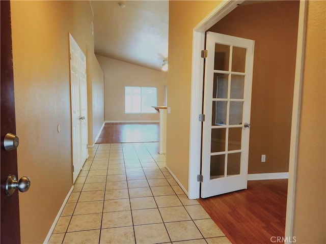 hall featuring lofted ceiling, light tile patterned floors, and baseboards