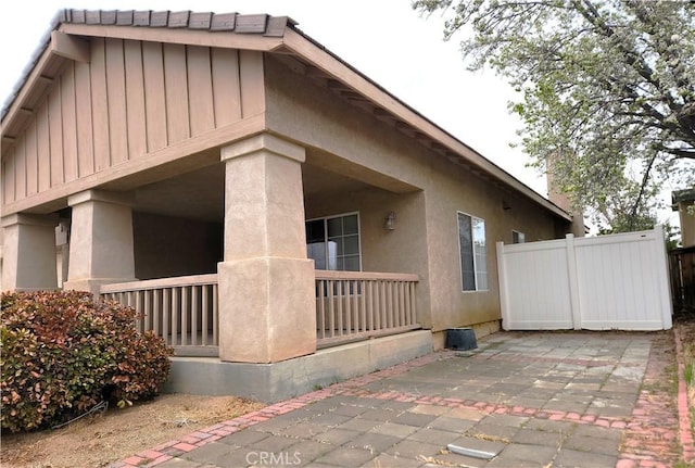 view of side of home featuring stucco siding, board and batten siding, a patio, and fence