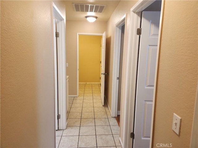 hallway with visible vents, light tile patterned flooring, and a textured wall