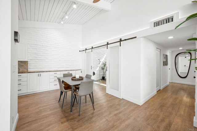 dining room featuring a barn door, visible vents, light wood-style flooring, and rail lighting