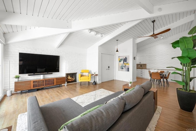 living area with a brick fireplace, brick wall, beam ceiling, wooden ceiling, and wood finished floors