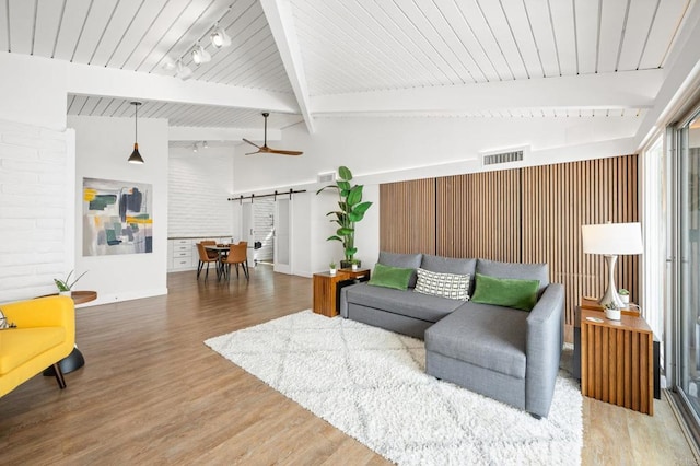 living room with a barn door, beamed ceiling, visible vents, and wood finished floors