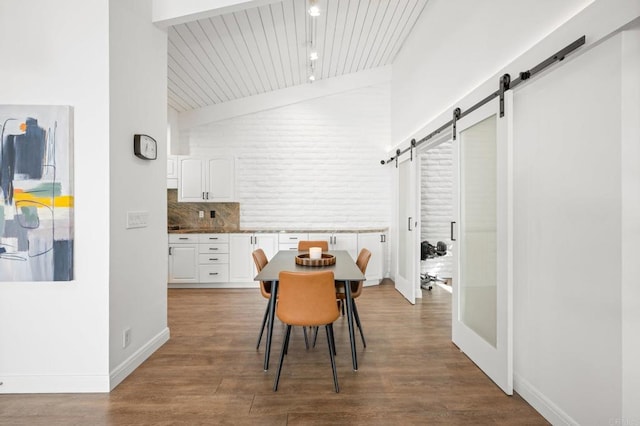 dining area with a barn door, wood finished floors, baseboards, and lofted ceiling