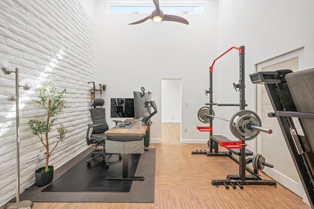 workout room featuring baseboards, a high ceiling, wood finished floors, and a ceiling fan